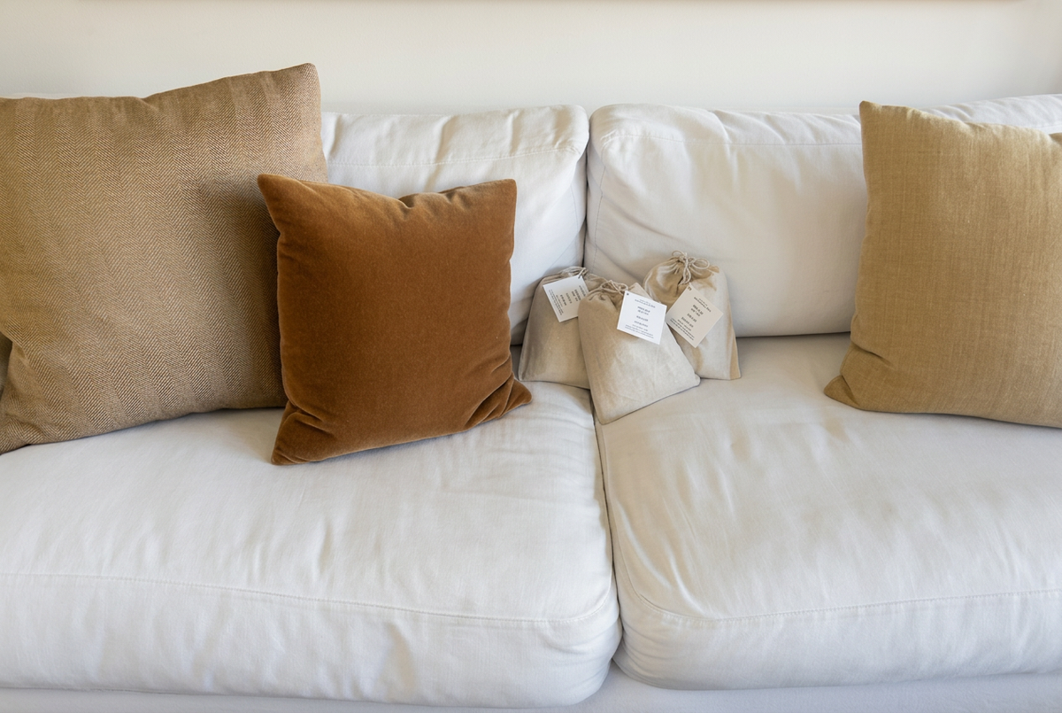 Three beige grounding bags with white printed tags on a white sofa between tan and brown cushions.