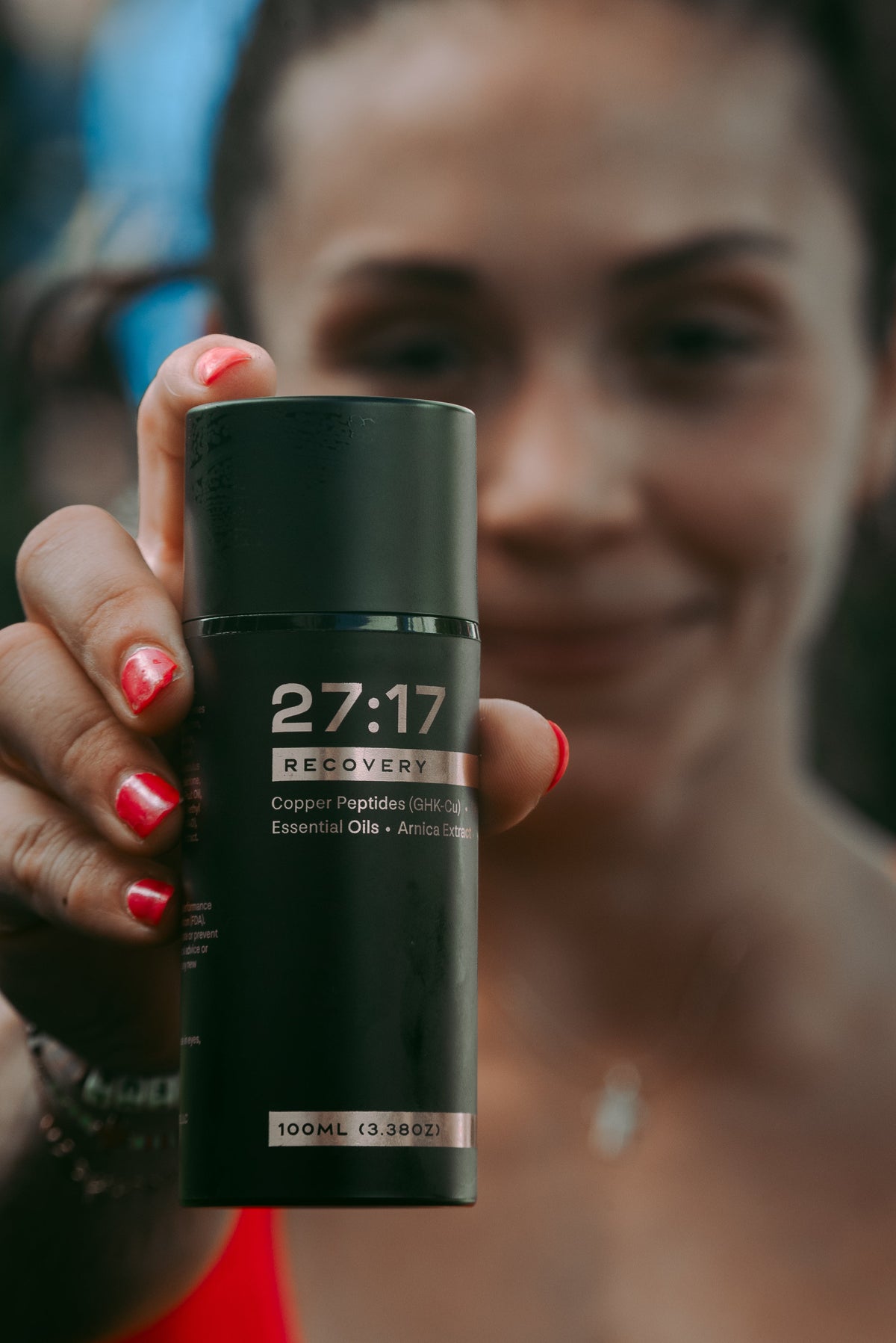 Professional CrossFit Athlete Fee Saghafi holding a black bottle of 27:17 Recovery Joint + Muscle Cream with a blurred background