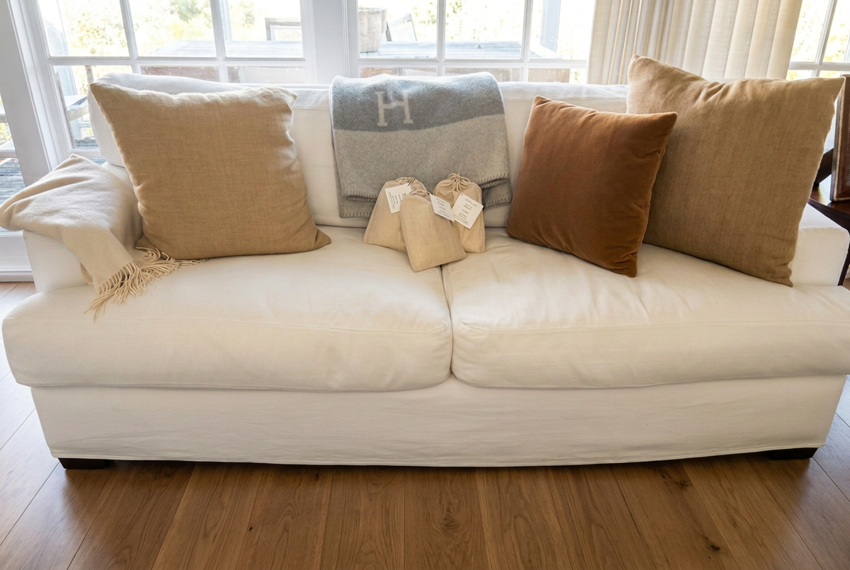Beige grounding bags centered on a white sofa with tan and brown cushions above a warm wood floor in a sunlit room.