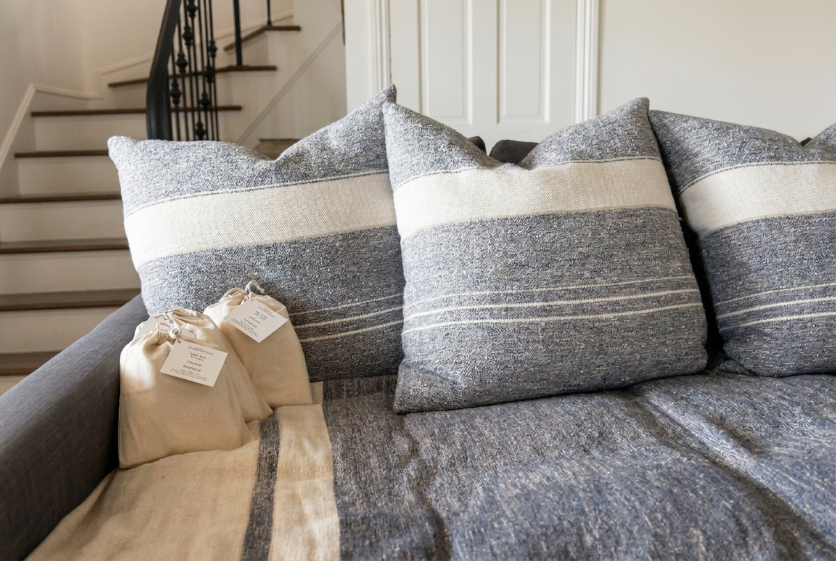Two beige grounding bags on a cream throw beside gray and cream striped cushions on a gray sofa.